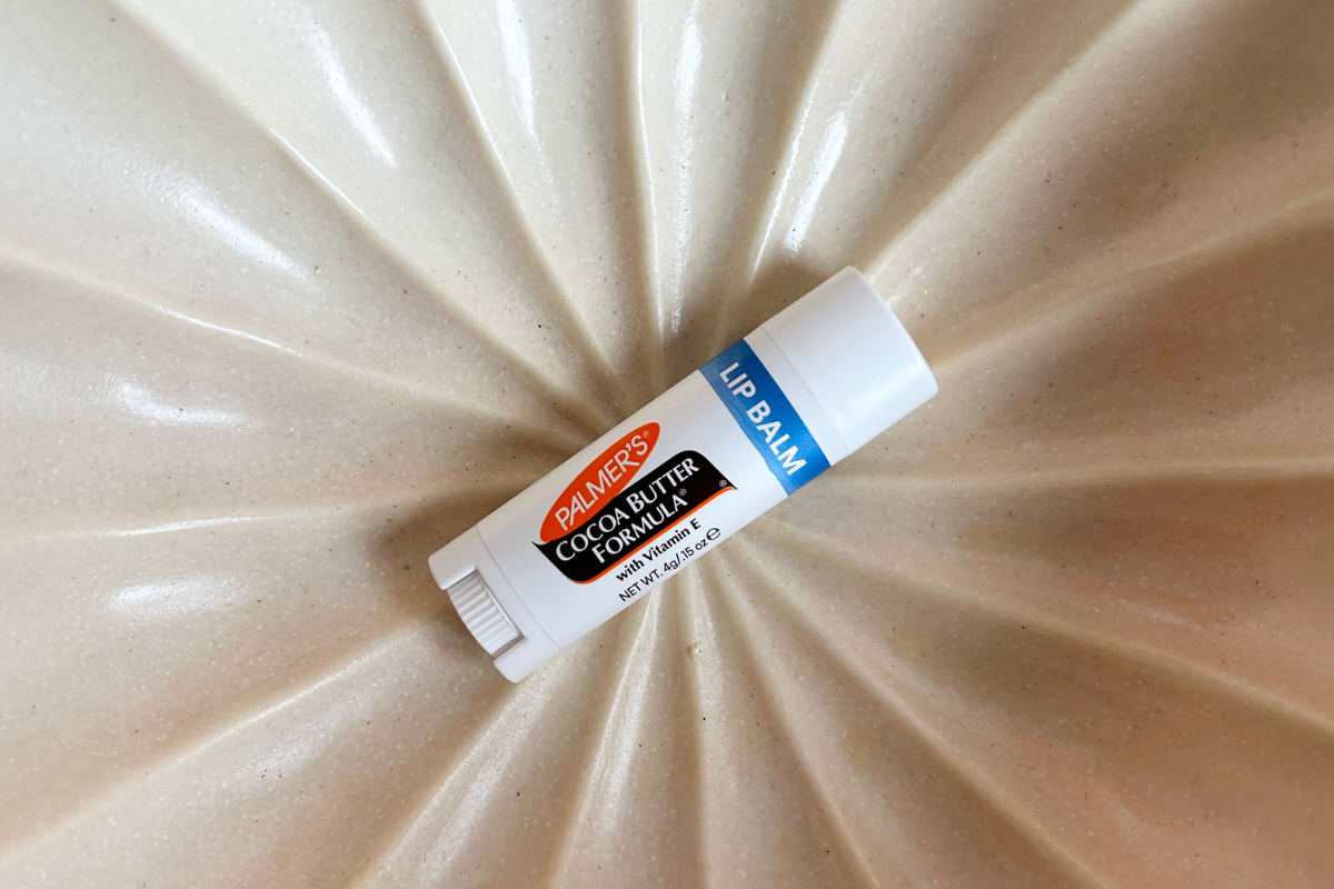 A tube of Palmer's Cocoa Butter Lip Balm shown laying on a white textured ceramic surface