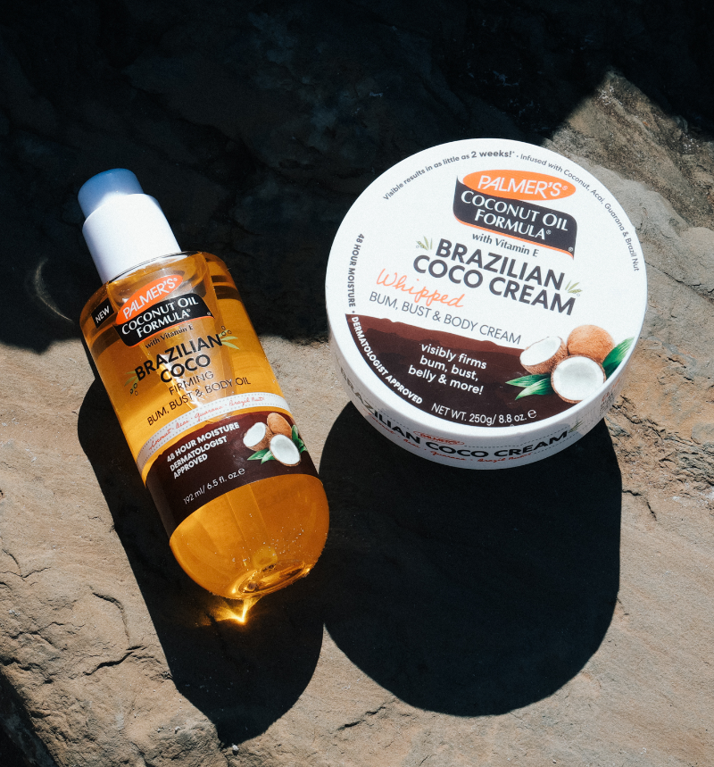 Palmer's Brazilian Coco Firming Body Oil bottle and Whipped Body Cream jar on a stone surface.
