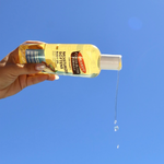 Hand holding a bottle of Palmer's Cocoa Butter Formula body oil against a blue sky.