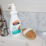 Palmer's Firms and Tones Body Lotion shown on a bathroom sink with a body brush