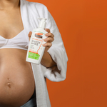 A pregnant woman holding a bottle of Palmer's Massage Lotions Stretch Marks lotion, set against a solid orange background.
