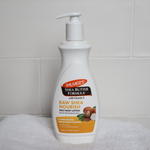 Palmer's Shea Butter Formula Raw Shea Nourish body lotion bottle on a towel with a tiled wall background