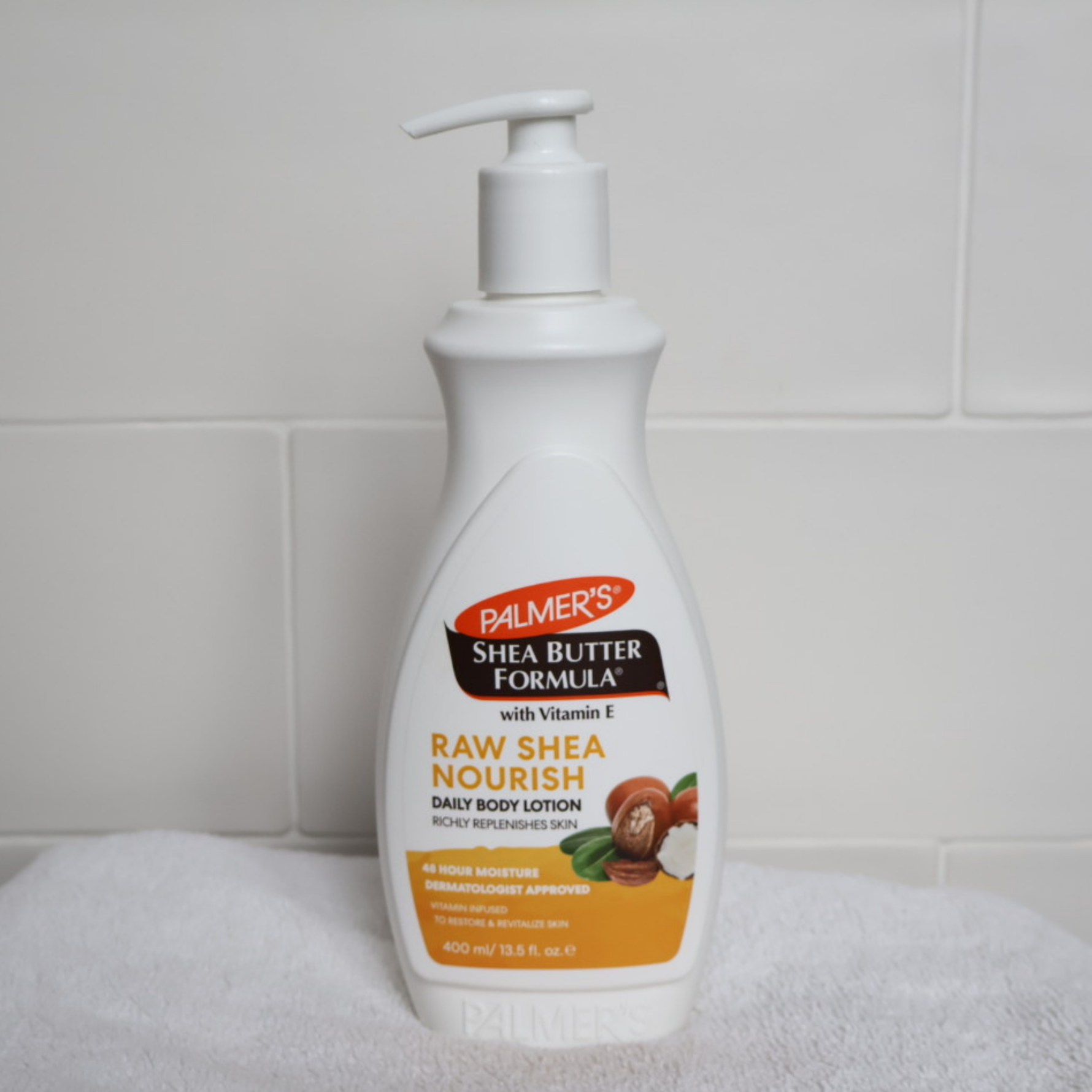 Palmer's Shea Butter Formula Raw Shea Nourish body lotion bottle on a towel with a tiled wall background