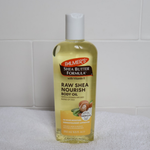 Palmer's Shea Butter Formula Raw Shea Nourish Body Oil bottle on a white towel with a tiled wall background