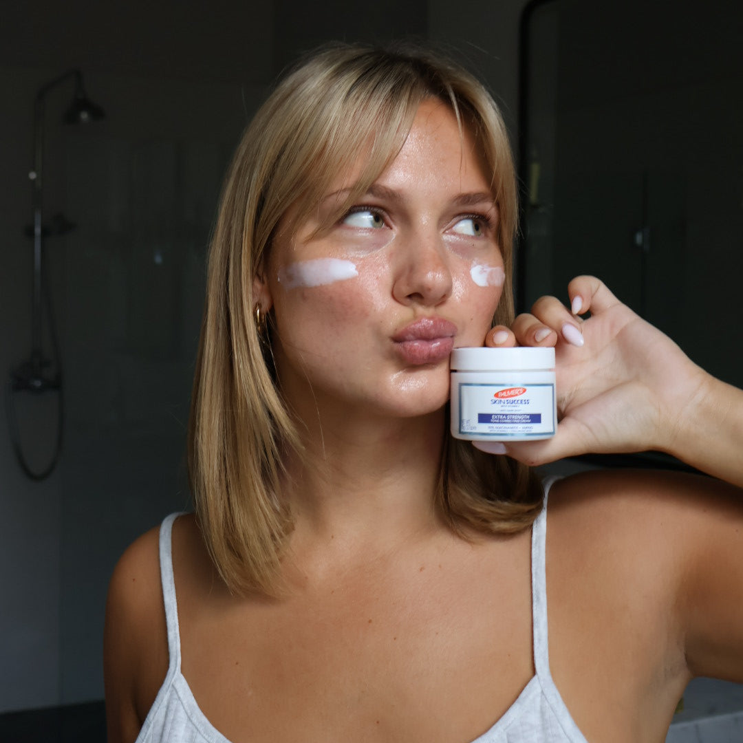 Woman applying Palmer's Skin Success Extra Strength Cream to her face with a bathroom background