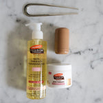 Palmer's Skin Therapy Cleansing Oil and Retinol-10 Cream flay lay on a marble bathroom counter top with aesthetic hair pin and blush stick