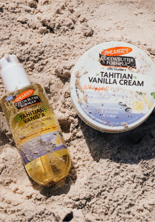 Palmers Tahitian Vanilla Whipped Body Cream and Body Oil bottle on sandy beach