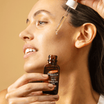 Woman applying a dropper of oil to her face with a bottle of Cocoa Butter Formula Skin Therapy Oil in front.