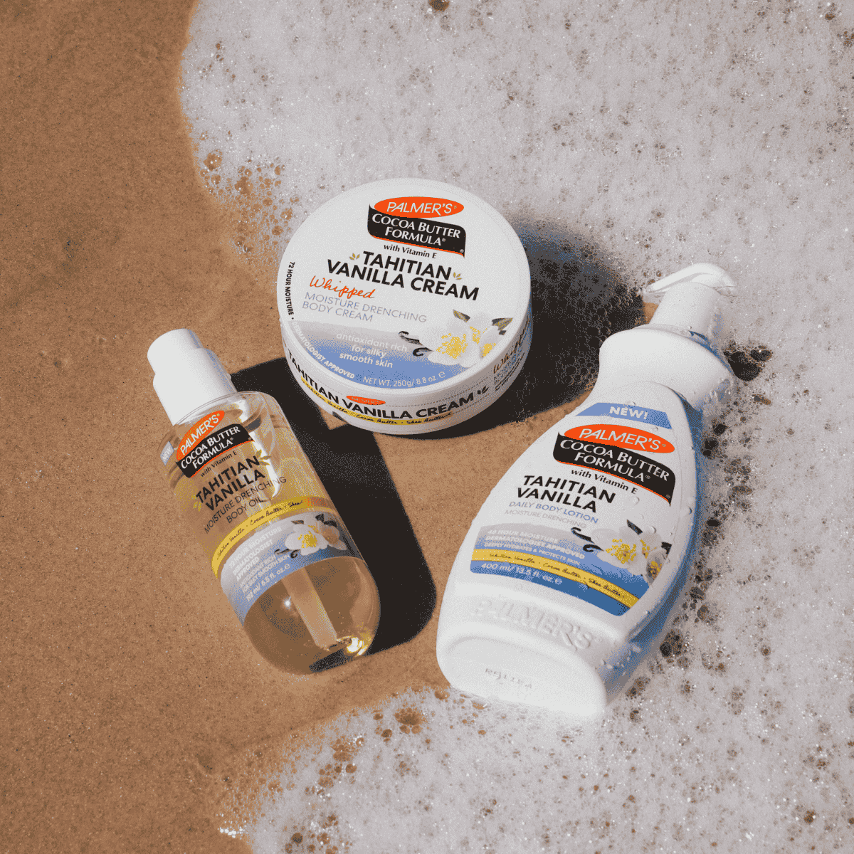 Three Palmers Tahitian Vanilla skincare products Body Lotion, Body Oil and Whipped Body Cream pictured washed up on a beach shore with sea foam and sand