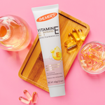 Palmer's Vitamin E cream tube on a pink background with capsules and a glass of liquid.