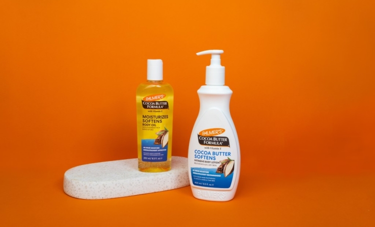 palmers cocoa butter body lotion and body oil on a bathroom tray with orange background
